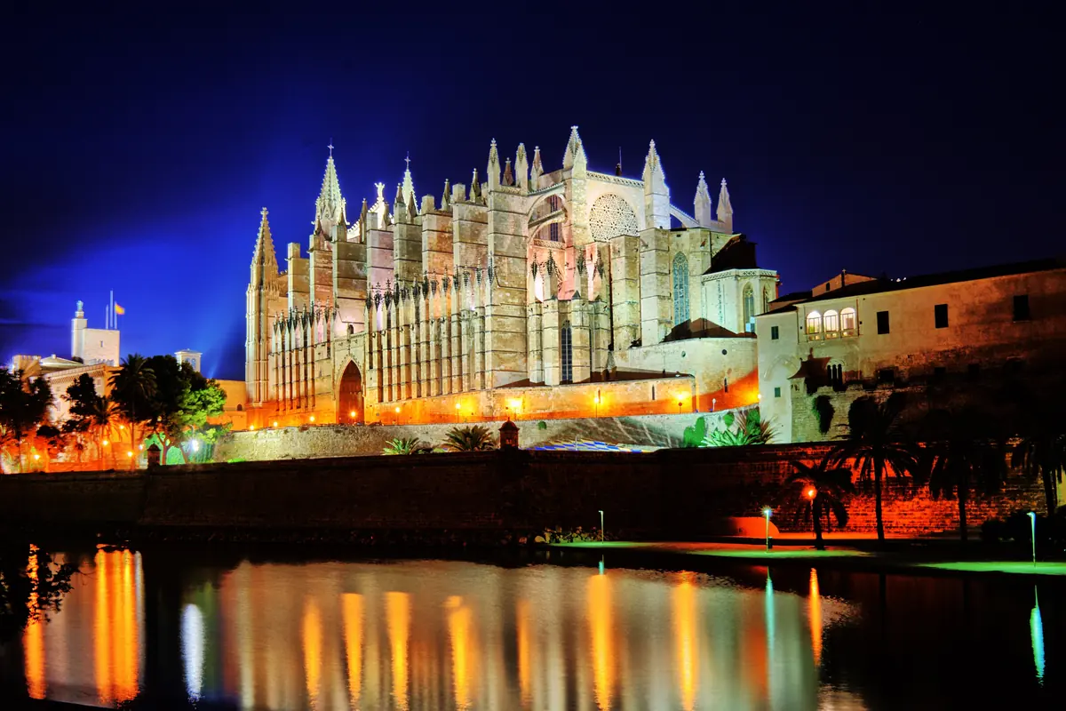 La Catedral de Palma iluminada contra un cielo nocturno azul profundo, reflejada en el agua frente a ella